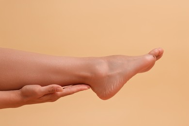 Photo of Woman touching her smooth feet on beige background, closeup