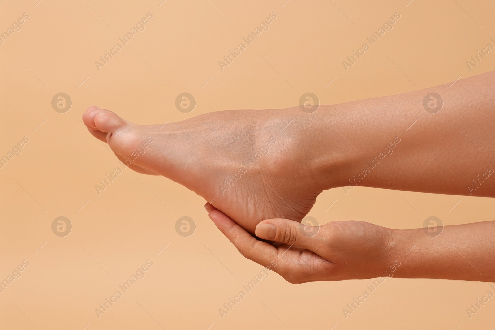 Photo of Woman touching her smooth feet on beige background, closeup