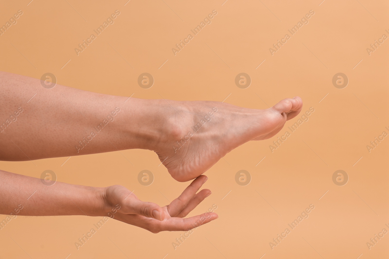 Photo of Woman touching her smooth feet on beige background, closeup