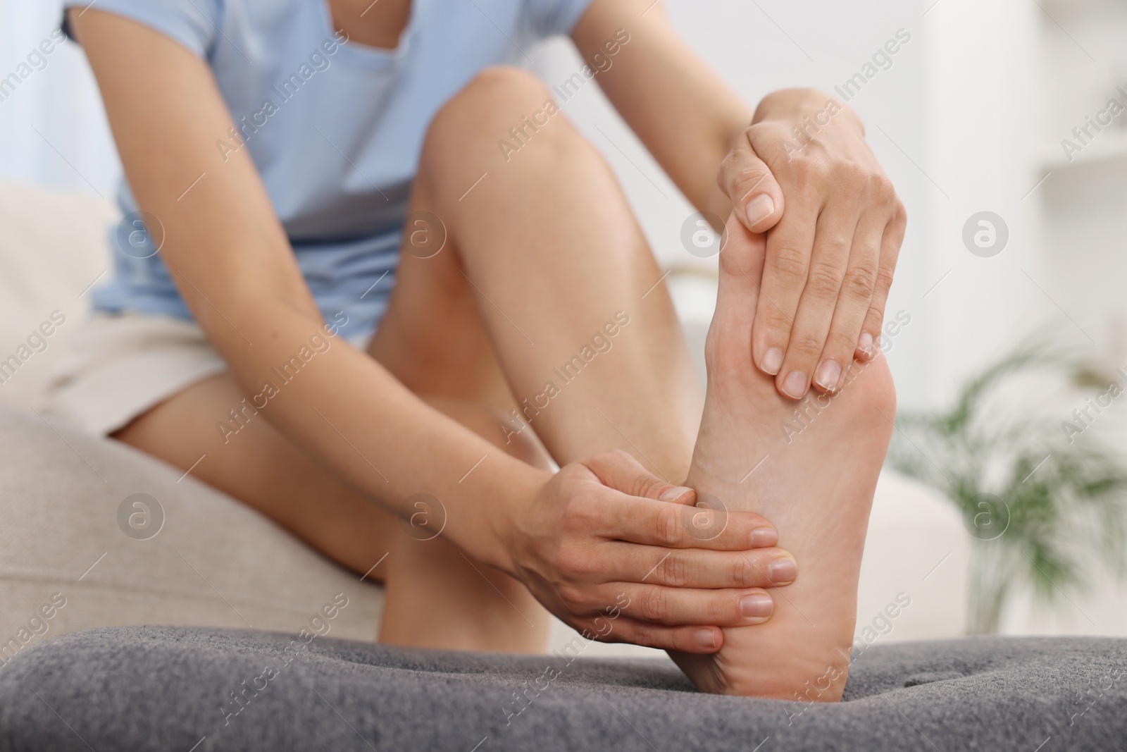 Photo of Woman suffering from foot pain at home, closeup