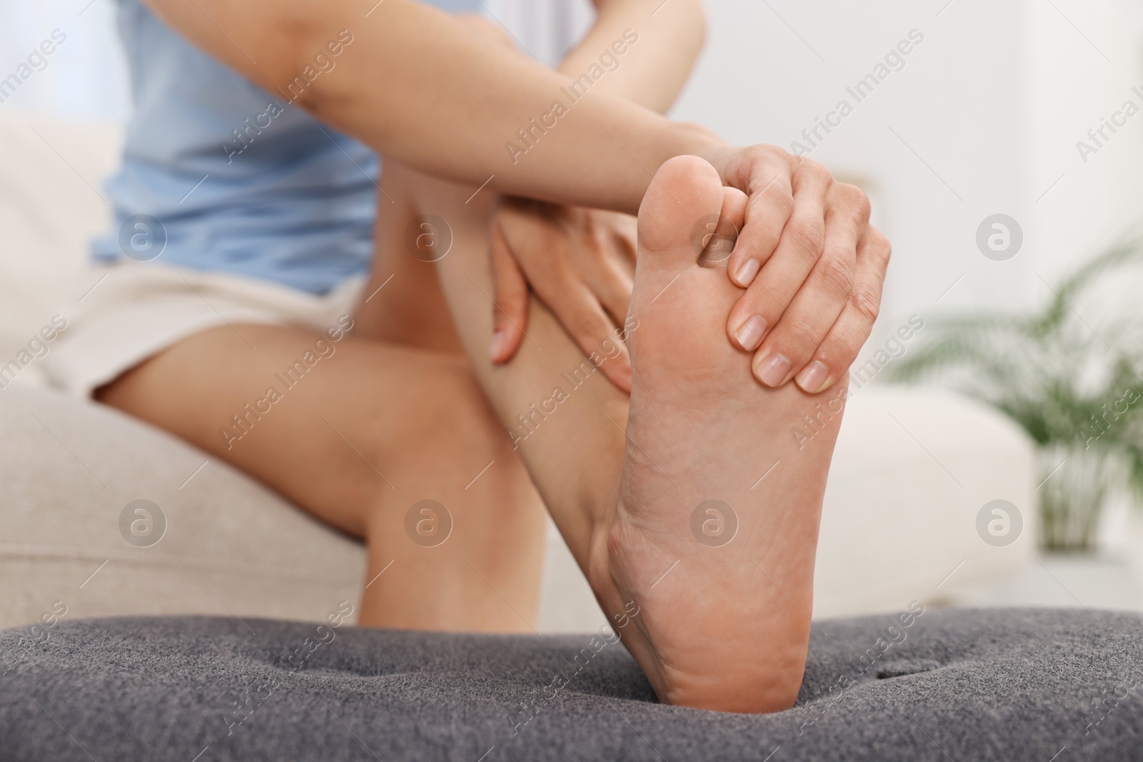 Photo of Woman suffering from foot pain at home, closeup