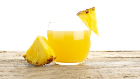 Photo of Tasty pineapple juice in glass and slices of fresh fruit on wooden table against white background