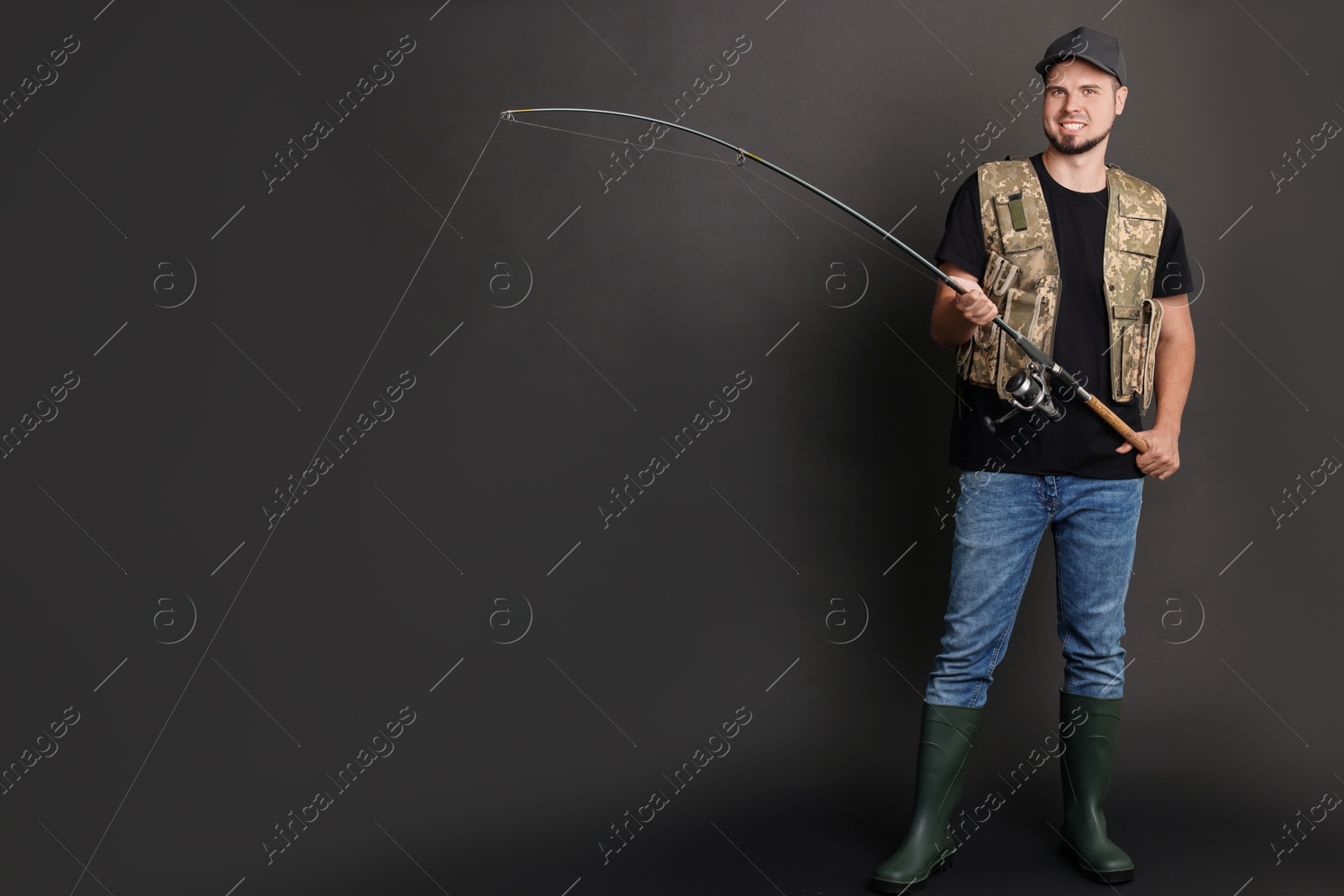 Photo of Smiling fisherman with rod fishing against black background