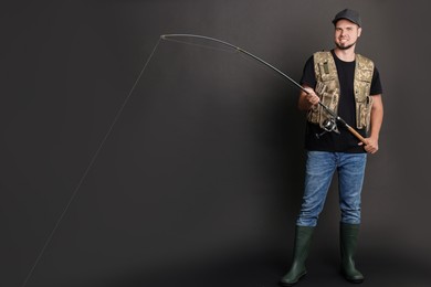 Smiling fisherman with rod fishing against black background