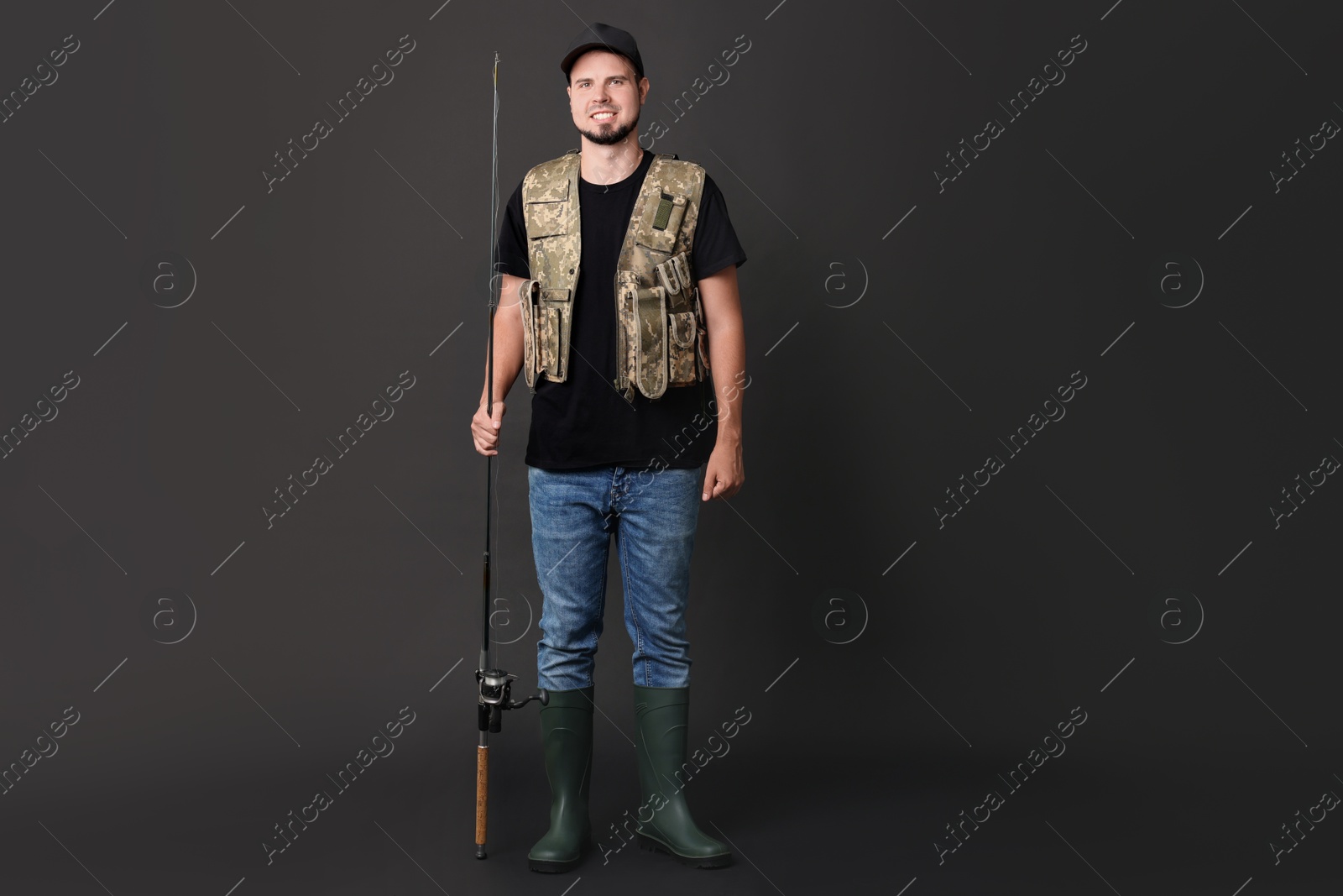 Photo of Smiling young fisherman with rod on black background