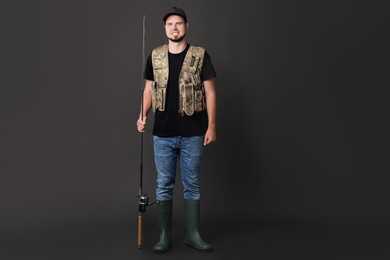 Photo of Smiling young fisherman with rod on black background