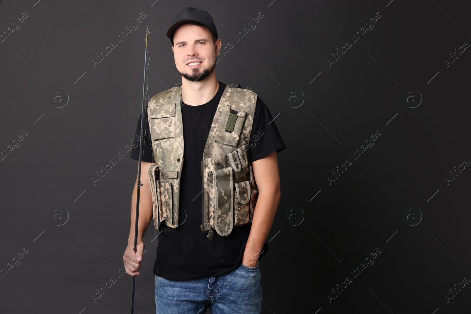 Photo of Smiling young fisherman with rod on black background