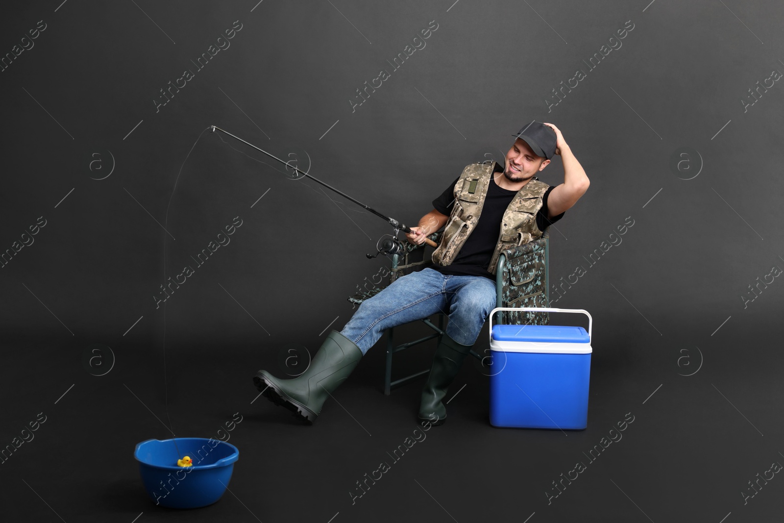 Photo of Fisherman with rod and cooler box fishing from bowl on chair against black background