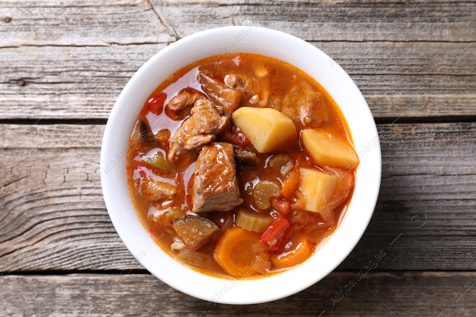 Photo of Delicious stew with vegetables in bowl on wooden table, top view