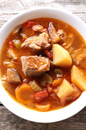 Delicious stew with vegetables in bowl on wooden table, top view