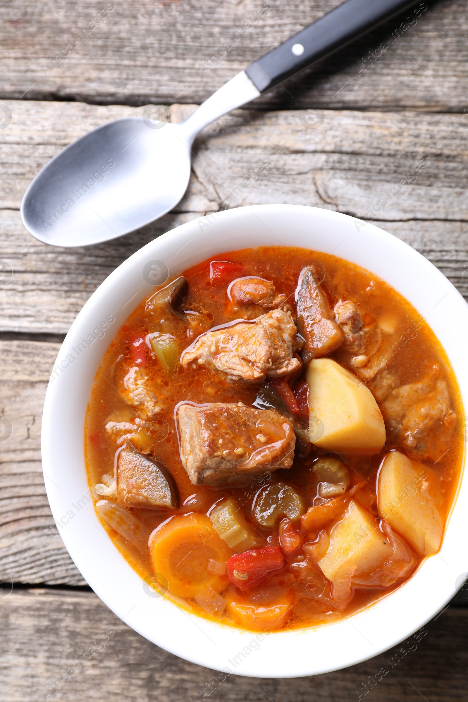 Photo of Delicious stew with vegetables in bowl and spoon on wooden table, top view