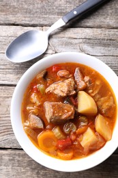 Photo of Delicious stew with vegetables in bowl and spoon on wooden table, top view