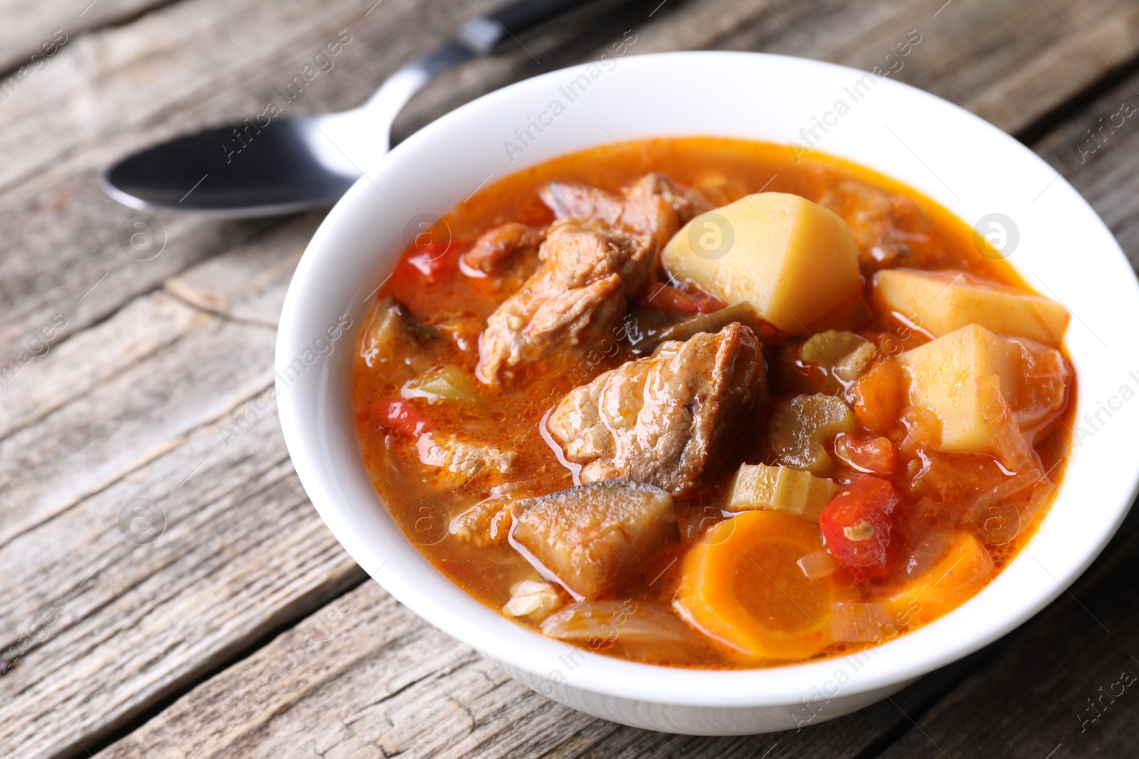 Photo of Delicious stew with vegetables in bowl and spoon on wooden table, closeup