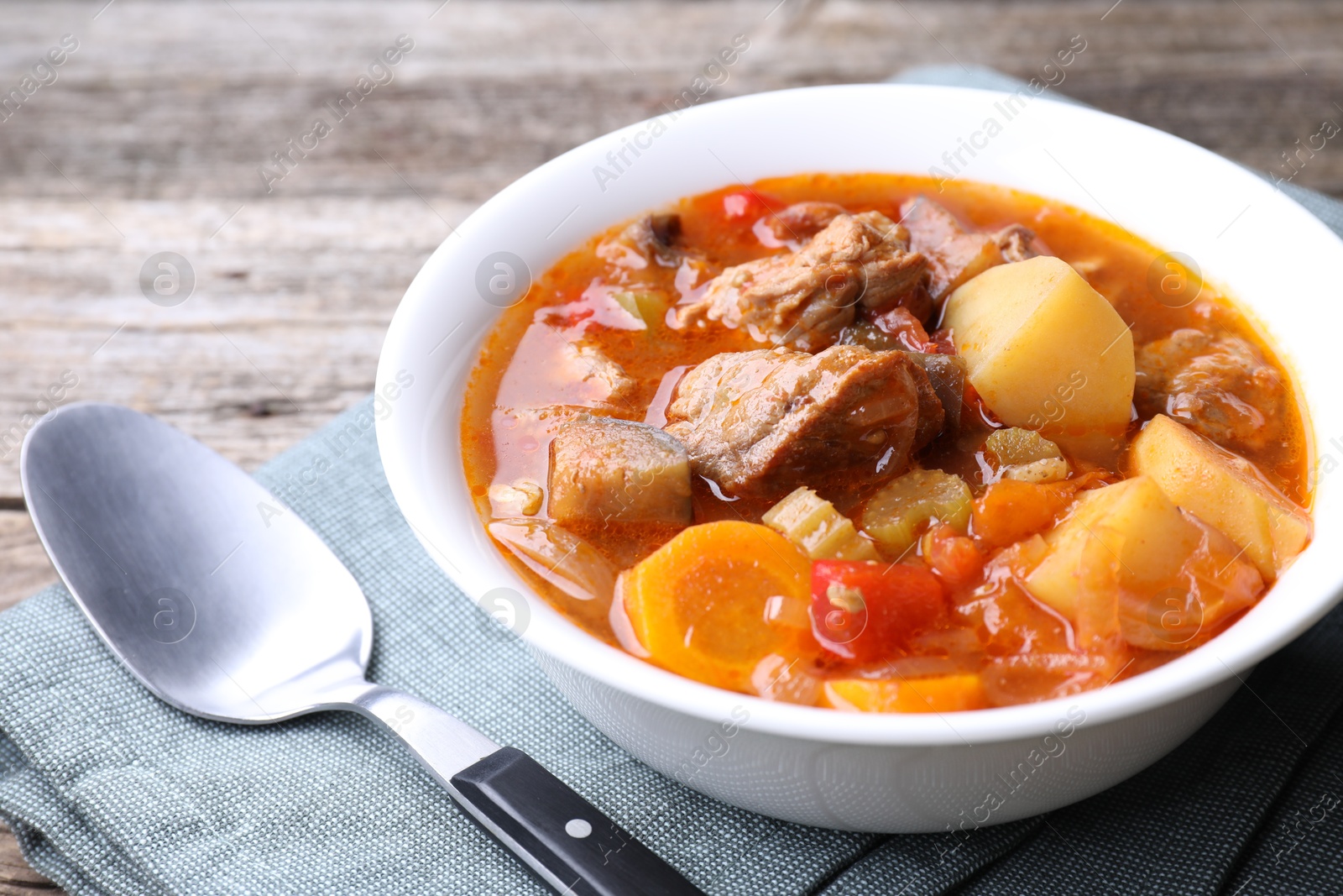 Photo of Delicious stew with vegetables in bowl and spoon on wooden table, closeup