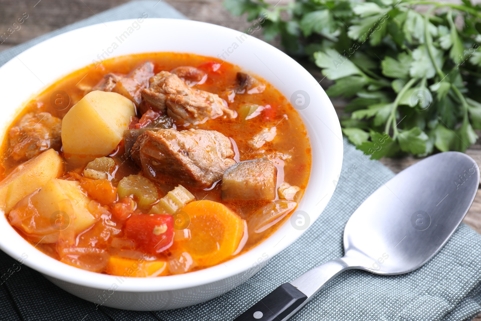 Photo of Delicious stew with vegetables in bowl, parsley and spoon on table, closeup