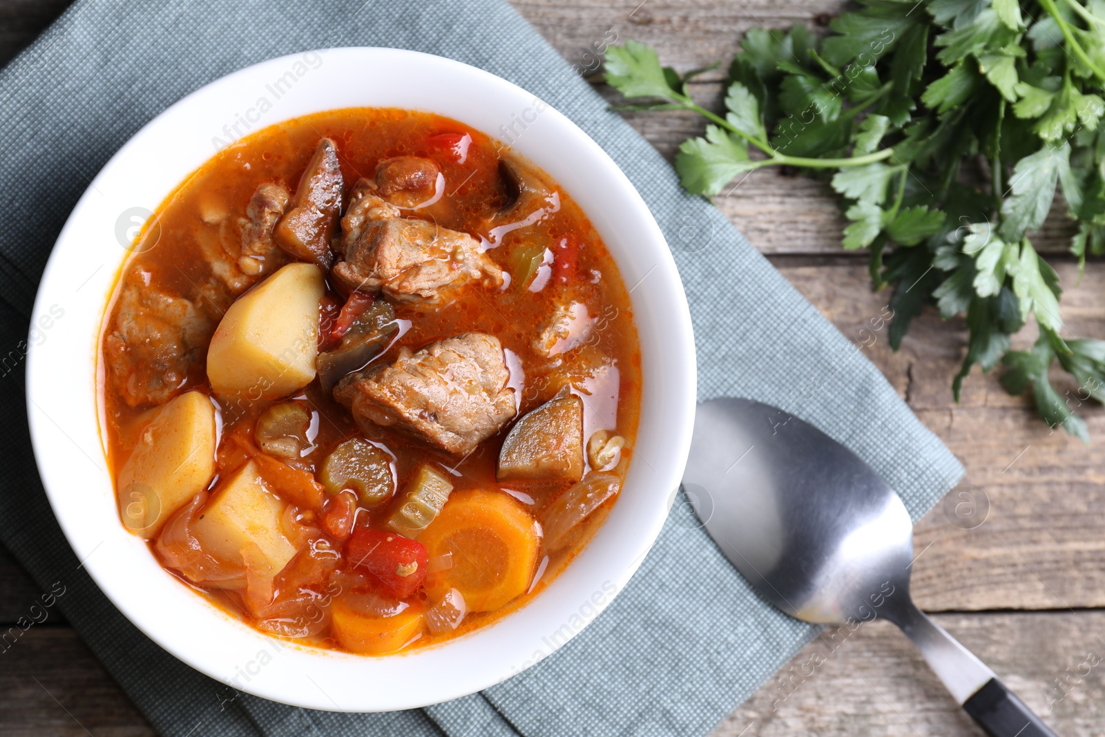 Photo of Delicious stew with vegetables in bowl, parsley and spoon on wooden table, top view