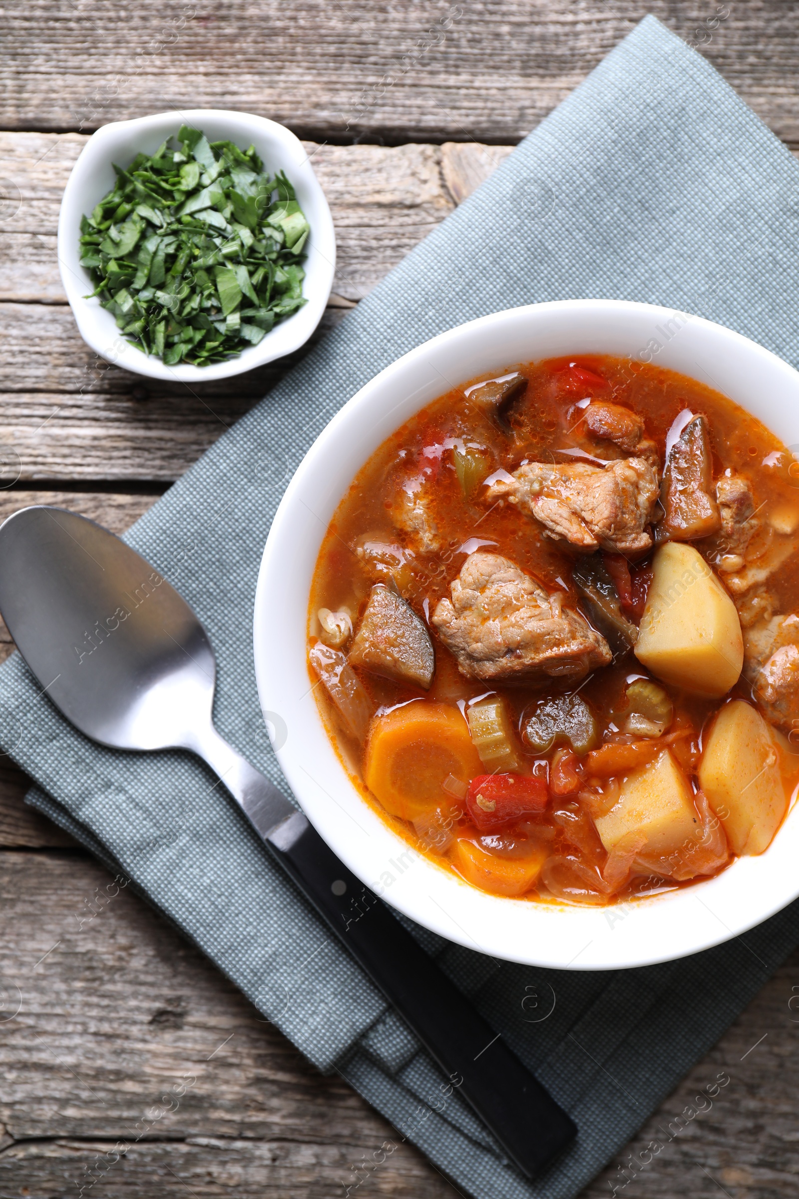 Photo of Delicious stew with vegetables in bowl, parsley and spoon on wooden table, top view