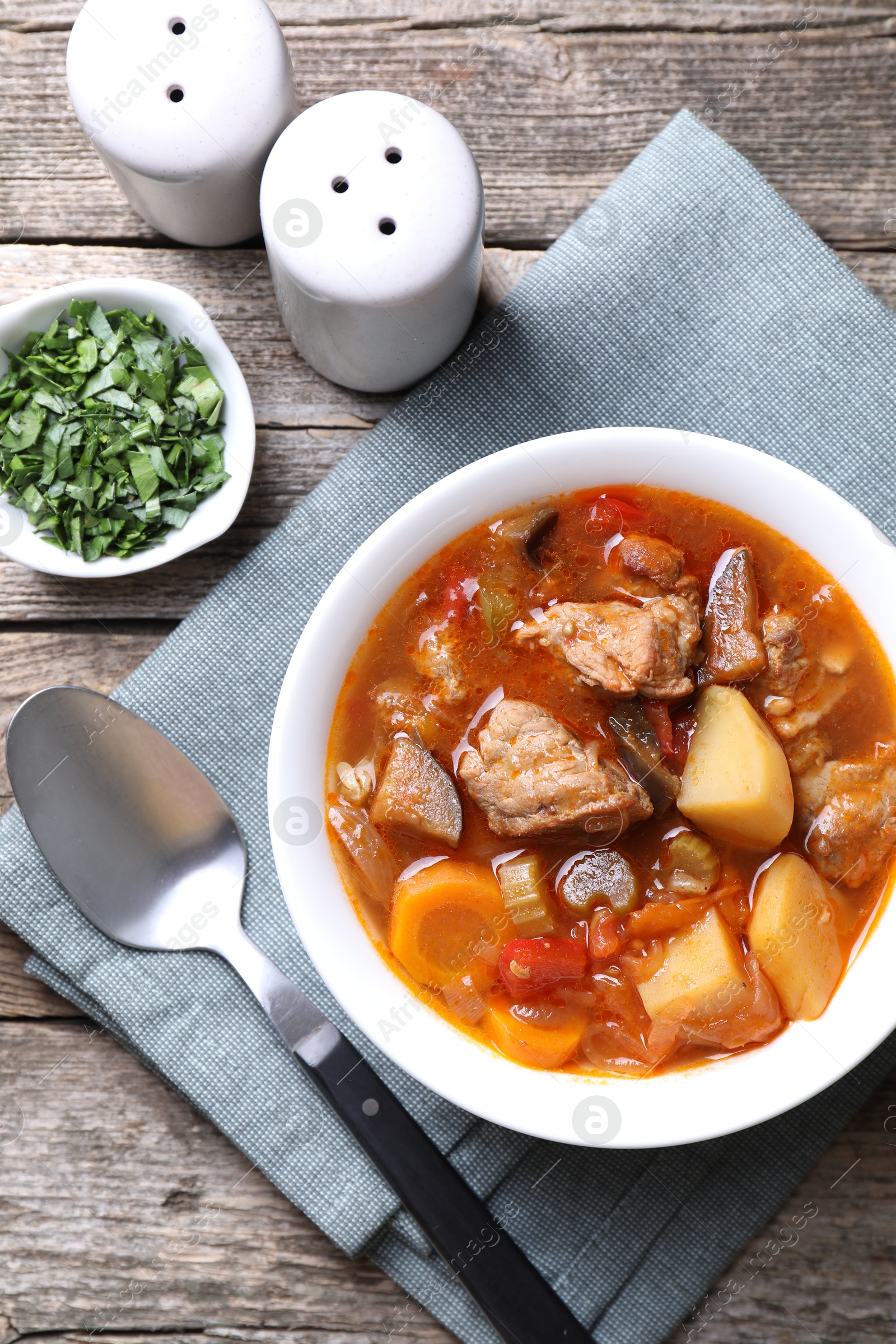 Photo of Delicious stew with vegetables in bowl, parsley and spoon on wooden table, top view