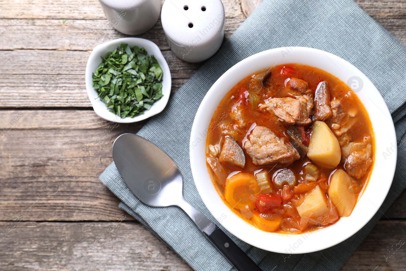 Photo of Delicious stew with vegetables in bowl, parsley and spoon on wooden table, top view