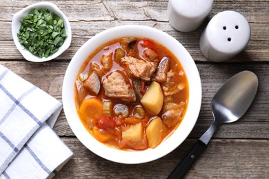 Delicious stew with vegetables in bowl, parsley and spoon on wooden table, top view