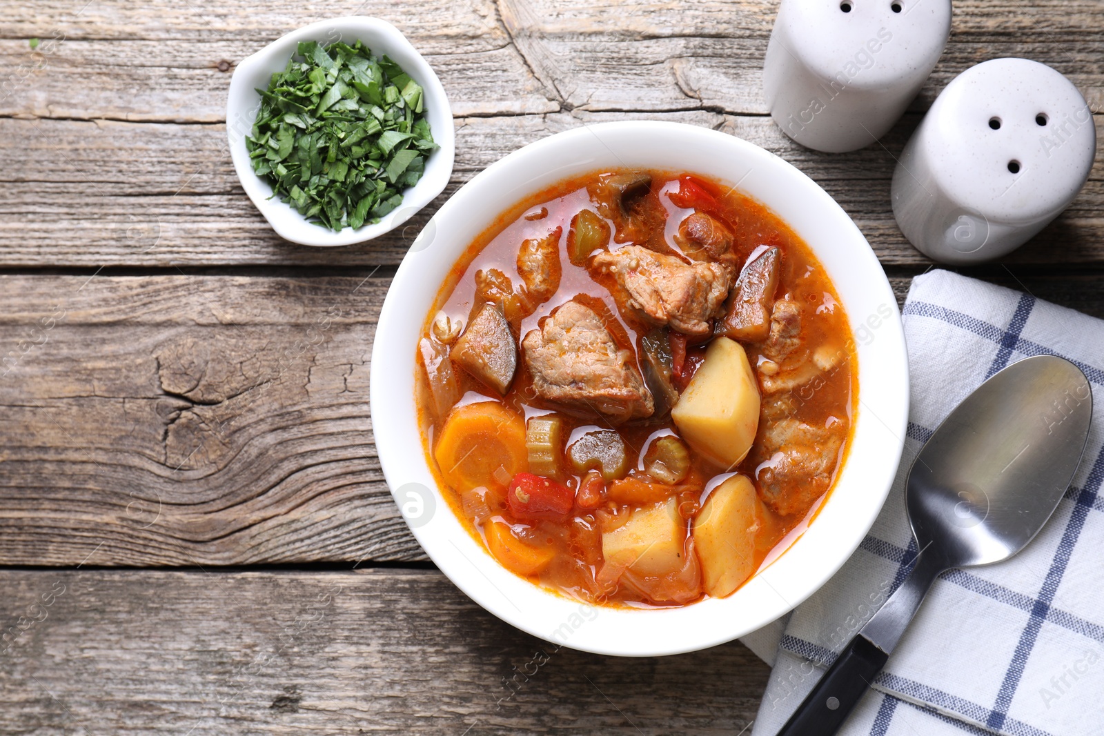 Photo of Delicious stew with vegetables in bowl, parsley and spoon on wooden table, top view