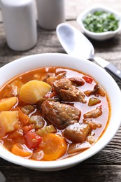 Delicious stew with vegetables in bowl on wooden table, closeup