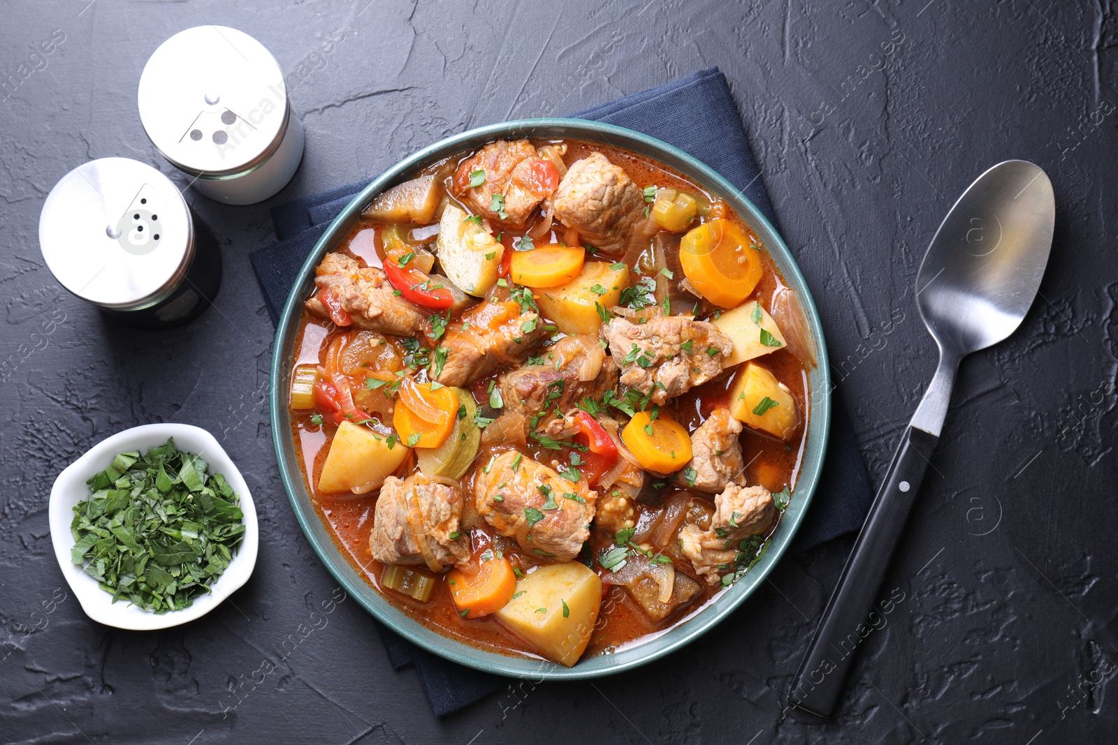 Photo of Delicious stew with vegetables, parsley and spoon on black table, top view