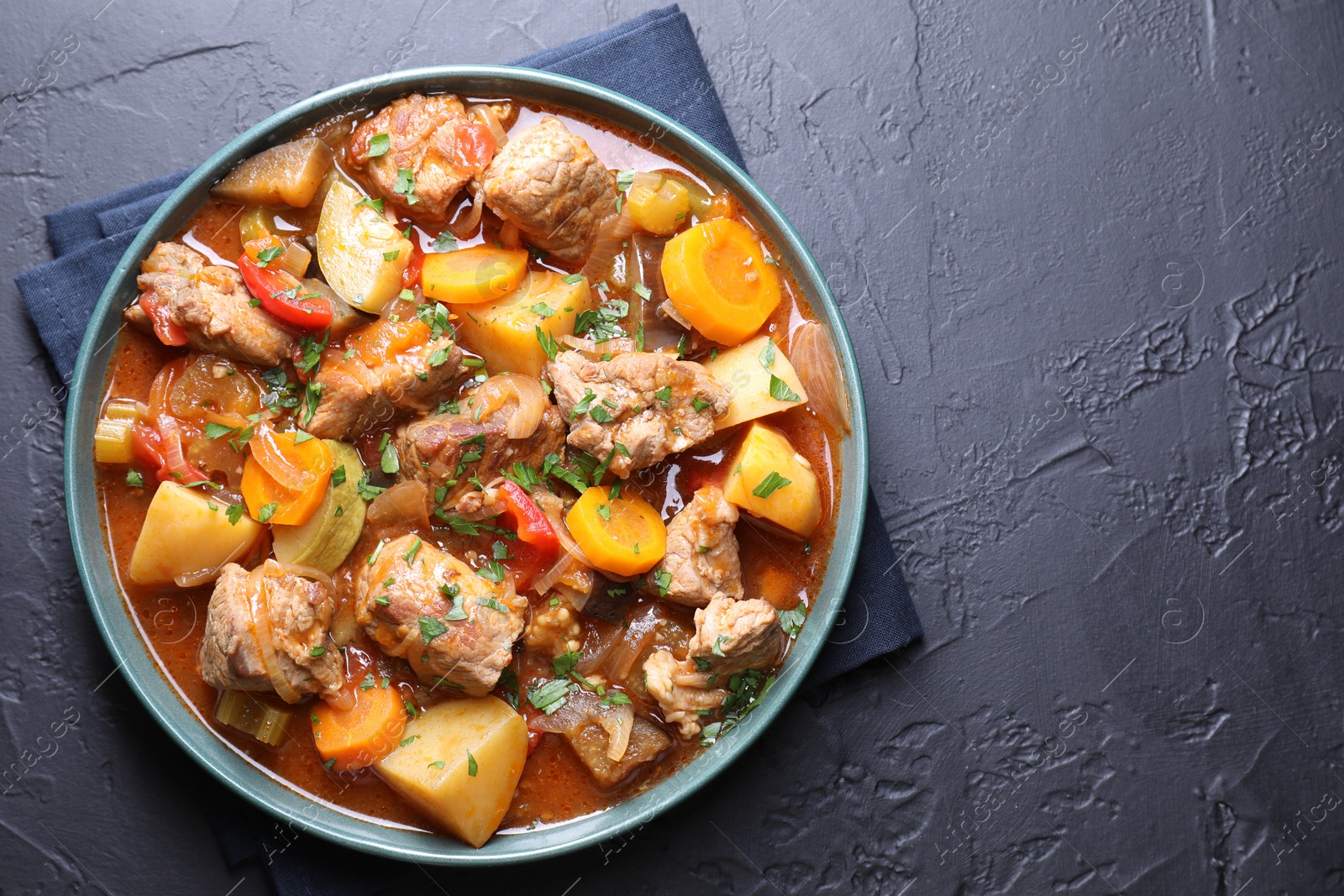 Photo of Delicious stew with vegetables on black table, top view. Space for text