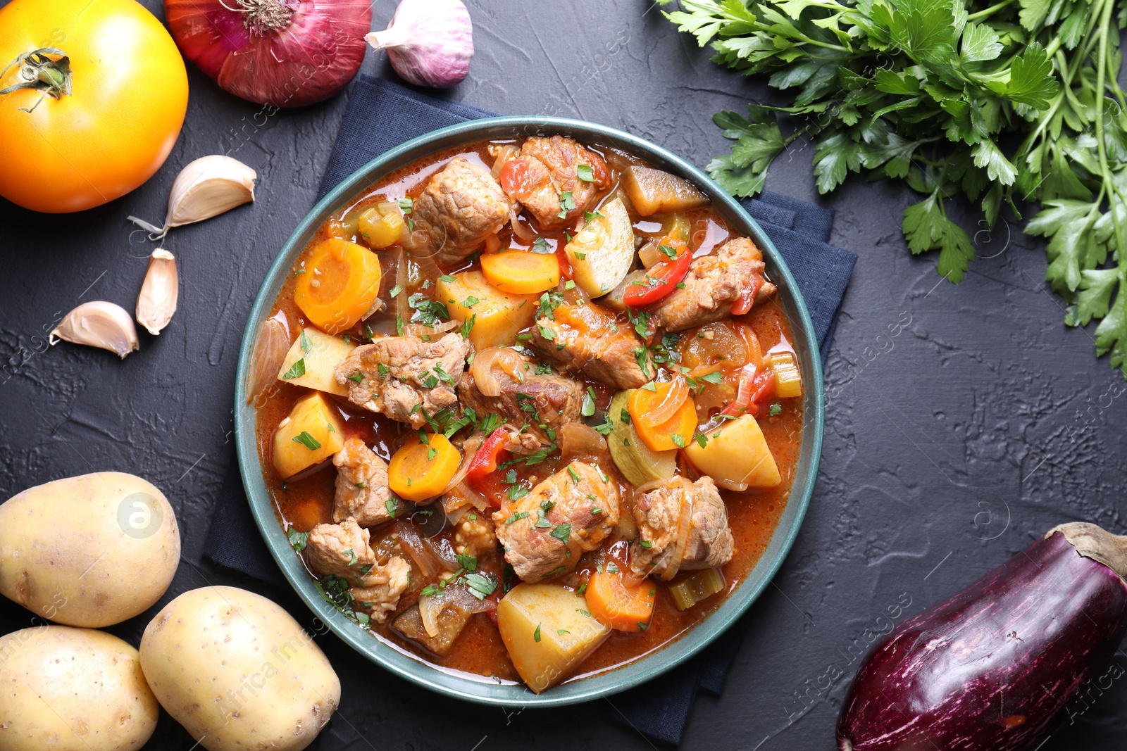 Photo of Delicious stew and different ingredients on black table, flat lay