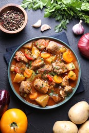 Photo of Delicious stew and different ingredients on black table, flat lay