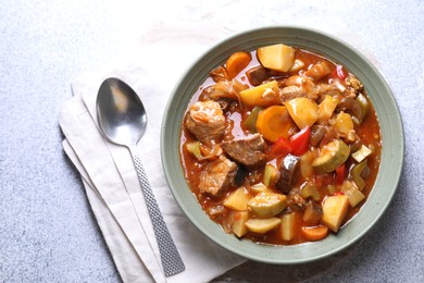 Photo of Delicious stew with vegetables in bowl and spoon on light grey table, top view