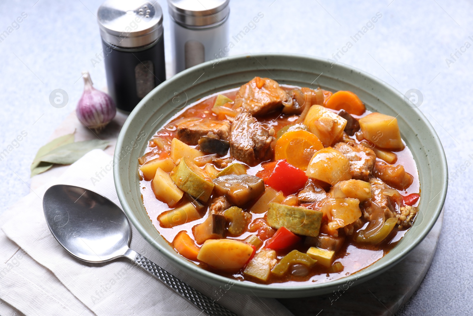 Photo of Delicious stew with vegetables in bowl, spices and spoon on table, closeup