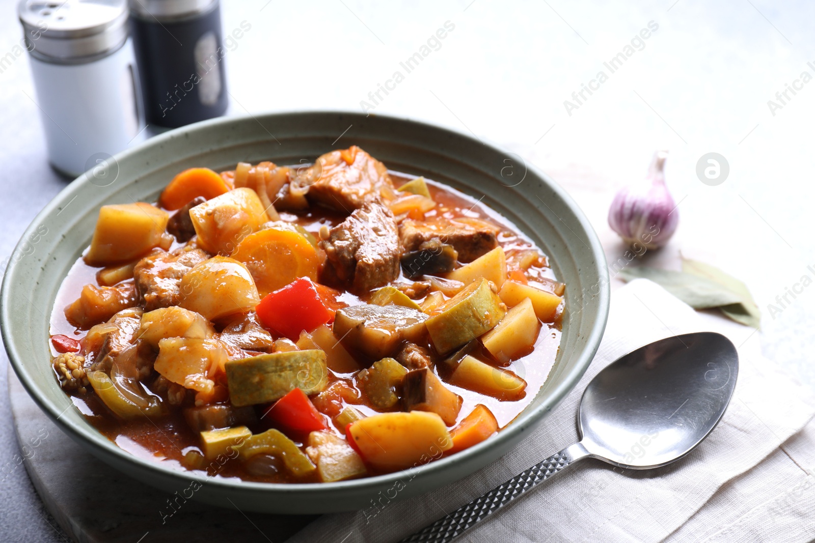 Photo of Delicious stew with vegetables in bowl, spices and spoon on table, closeup