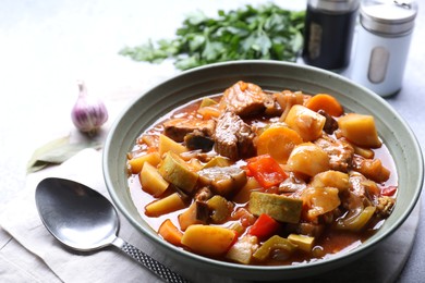 Photo of Delicious stew with vegetables in bowl, spices and spoon on table, closeup