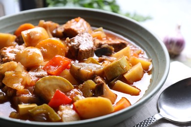 Photo of Delicious stew with vegetables in bowl and spoon on table, closeup