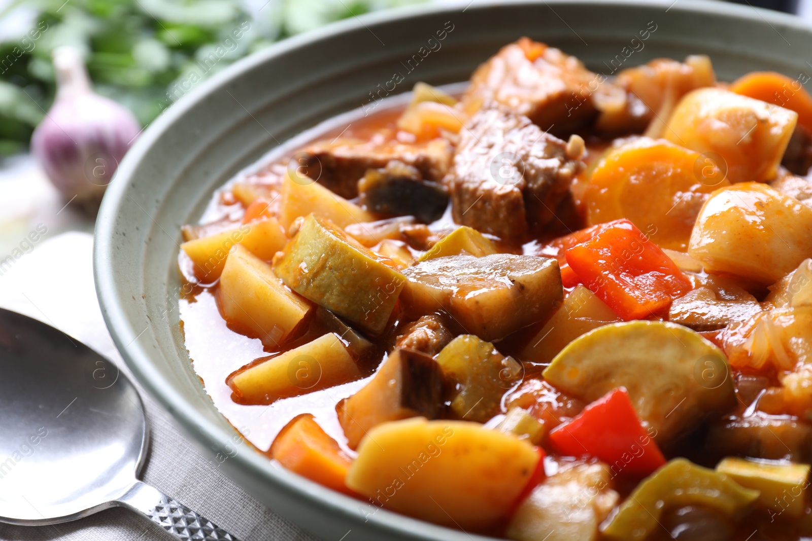 Photo of Delicious stew with vegetables in bowl and spoon on table, closeup