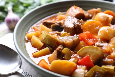 Delicious stew with vegetables in bowl and spoon on table, closeup