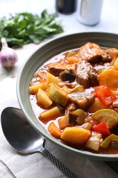 Photo of Delicious stew with vegetables in bowl and spoon on table, closeup