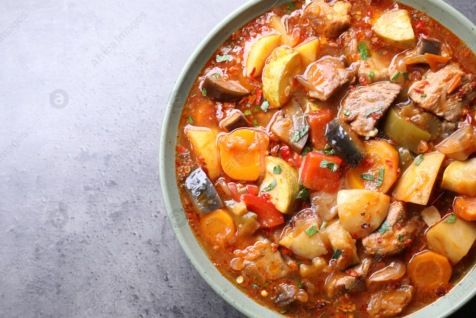 Photo of Delicious stew with vegetables in bowl on grey table, top view