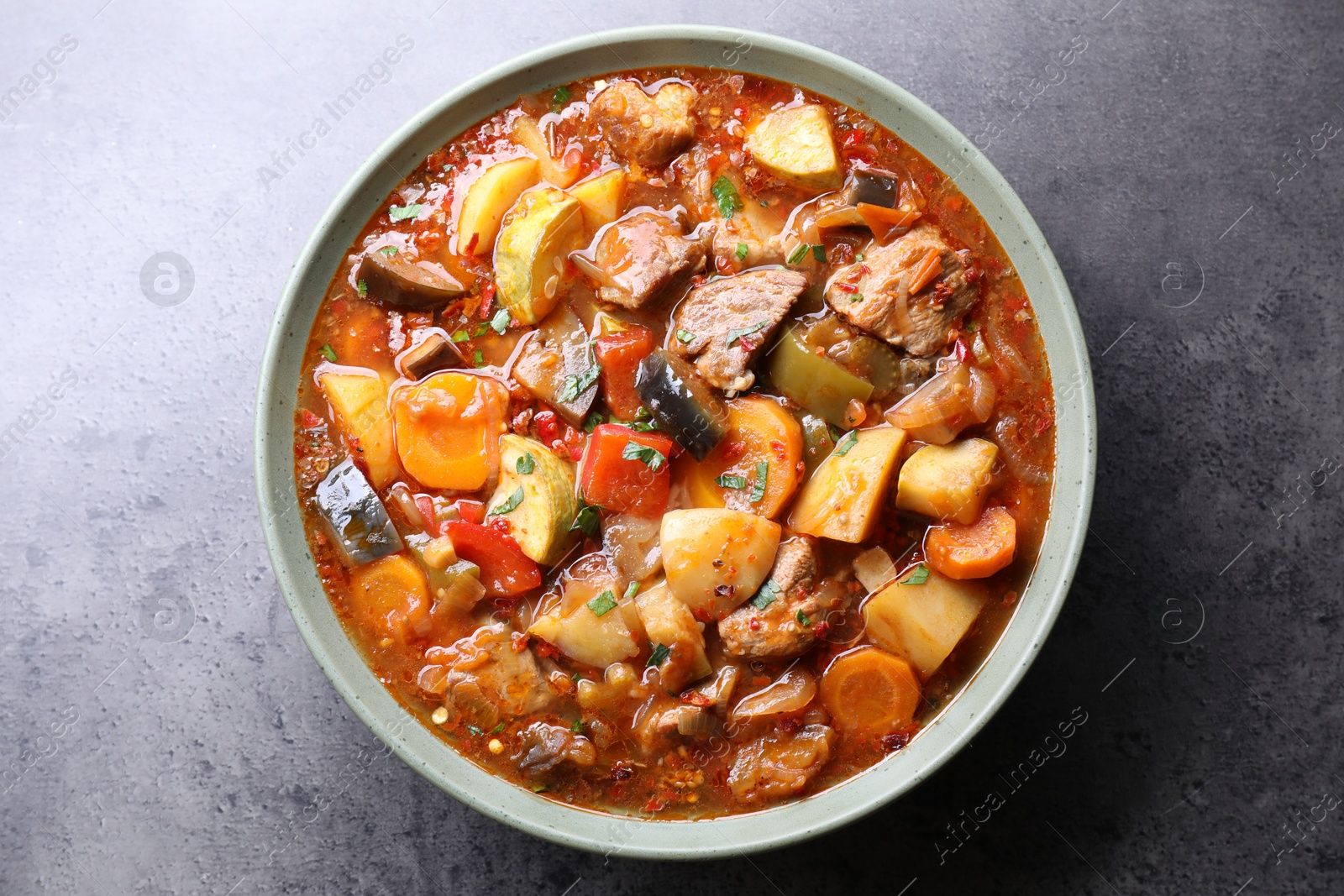 Photo of Delicious stew with vegetables in bowl on grey table, top view