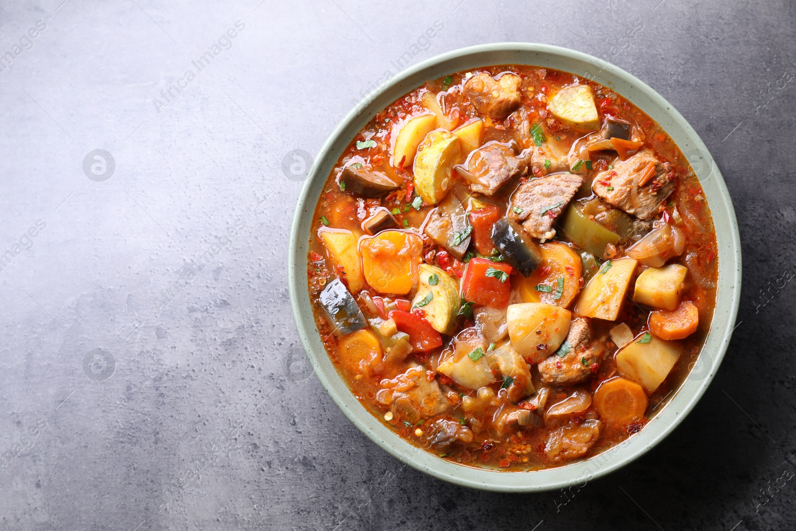 Photo of Delicious stew with vegetables in bowl on grey table, top view. Space for text