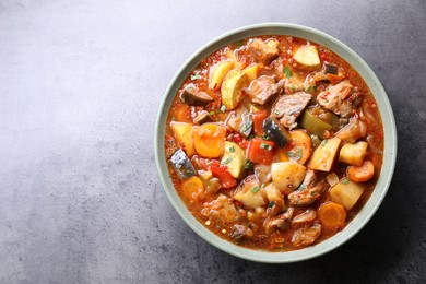 Photo of Delicious stew with vegetables in bowl on grey table, top view. Space for text