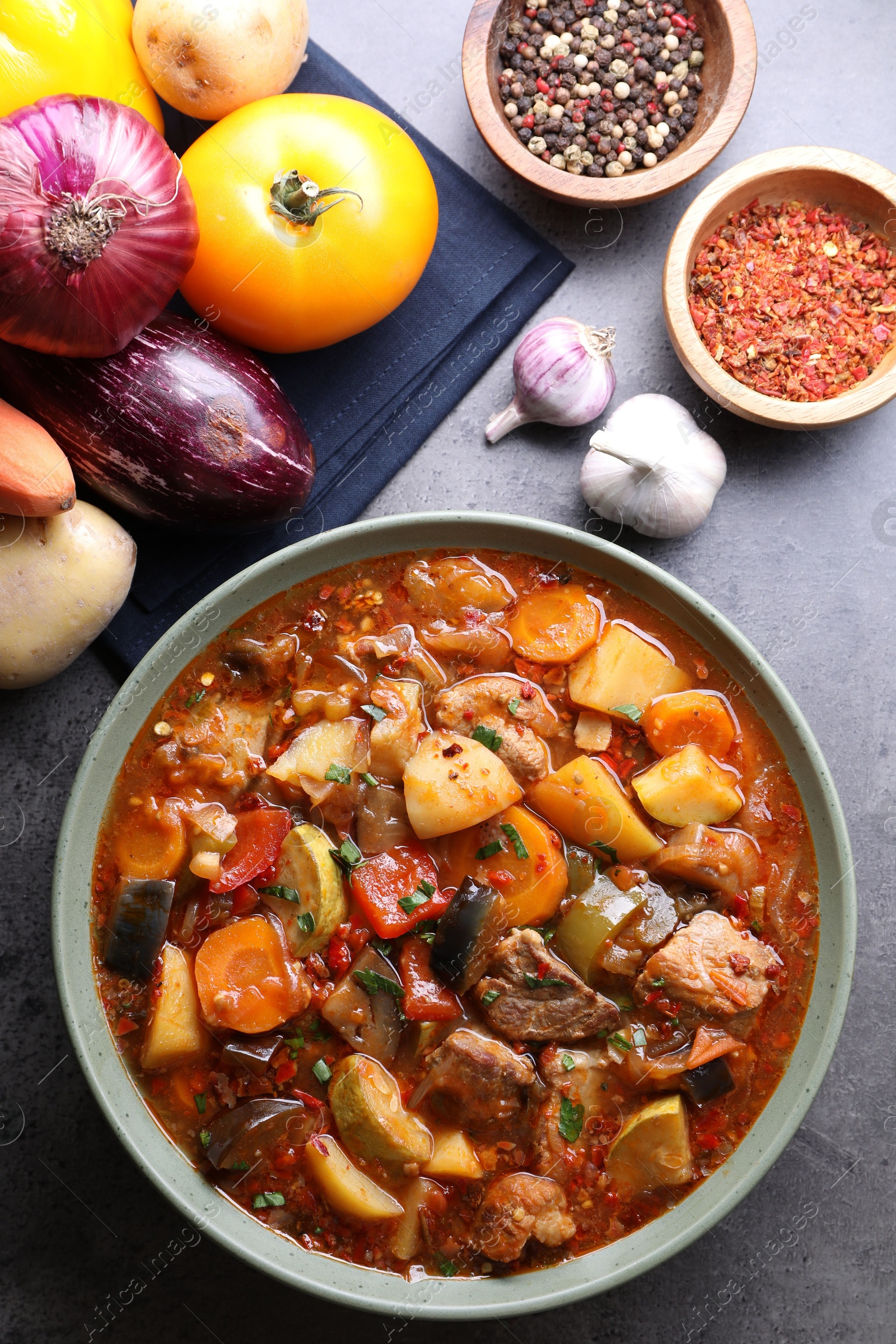 Photo of Delicious stew with vegetables in bowl and ingredients on grey table, flat lay