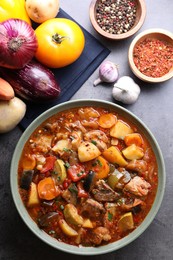 Photo of Delicious stew with vegetables in bowl and ingredients on grey table, flat lay