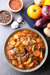 Photo of Delicious stew with vegetables in bowl and ingredients on grey table, flat lay