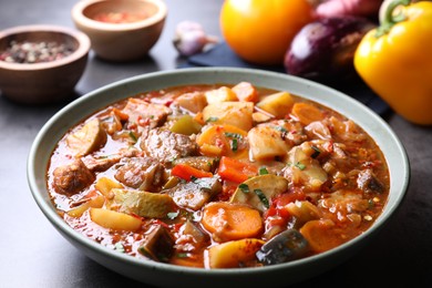 Photo of Delicious stew with vegetables in bowl and ingredients on grey table, closeup