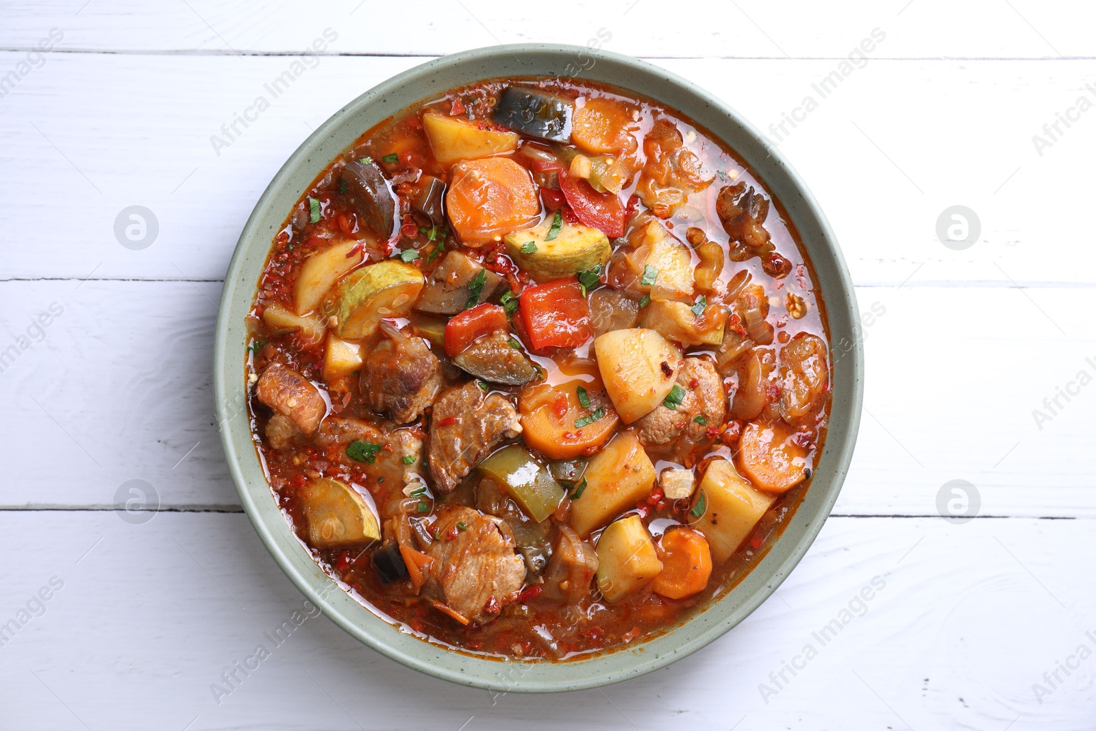 Photo of Delicious stew with vegetables in bowl on white wooden table, top view