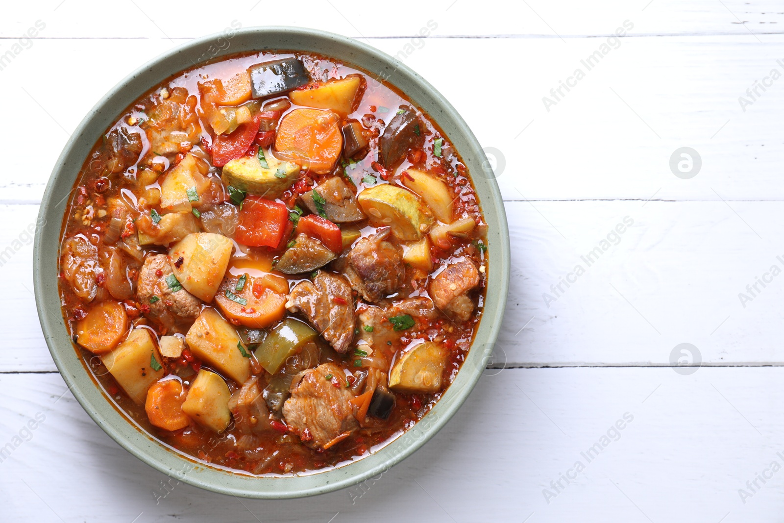 Photo of Delicious stew with vegetables in bowl on white wooden table, top view. Space for text