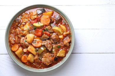 Delicious stew with vegetables in bowl on white wooden table, top view. Space for text