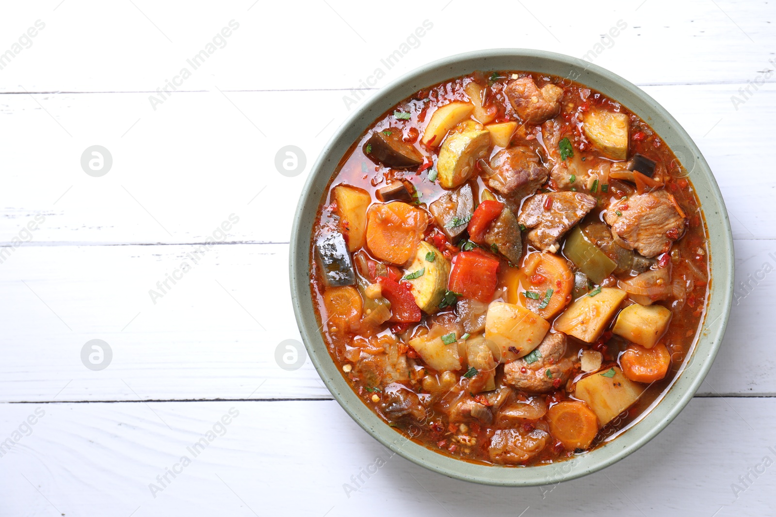 Photo of Delicious stew with vegetables in bowl on white wooden table, top view. Space for text